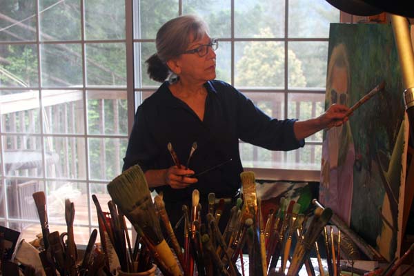 artist in studio with brushes easel paintings large window view of mountains