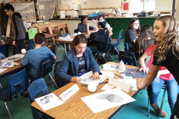 person, jars of paint brushes, easel with painting, window with view of deck, table, redwoods